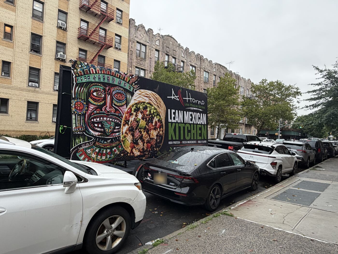 A Seen trailer with the Al Horno Lean Mexican Kitchen billboard parked on a Brooklyn street